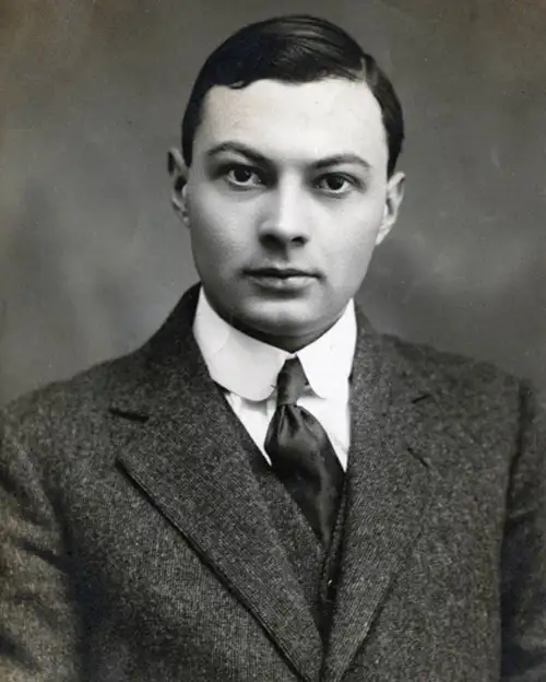Black-and-white studio portrait of a young clean-shaven man in a tweed jacket and dark tie.