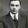 Black-and-white studio portrait of a young clean-shaven man in a tweed jacket and dark tie.