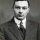 Black-and-white studio portrait of a young clean-shaven man in a tweed jacket and dark tie.