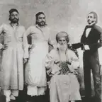 Black-and-white group photograph of an elderly bearded man in a turban, seated, with three men standing beside him.