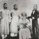 Black-and-white group photograph of an elderly bearded man in a turban, seated, with three men standing beside him.