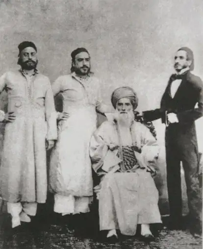 Black-and-white group photograph of an elderly bearded man in a turban, seated, with three men standing beside him.