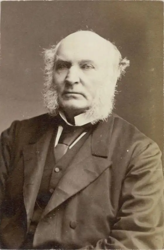 Sepia studio portrait of an elderly man with white mutton-chop whiskers, wearing a dark coat.