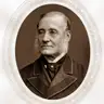 Sepia oval portrait of an elderly man with white side-whiskers in a dark coat with a velvet collar.