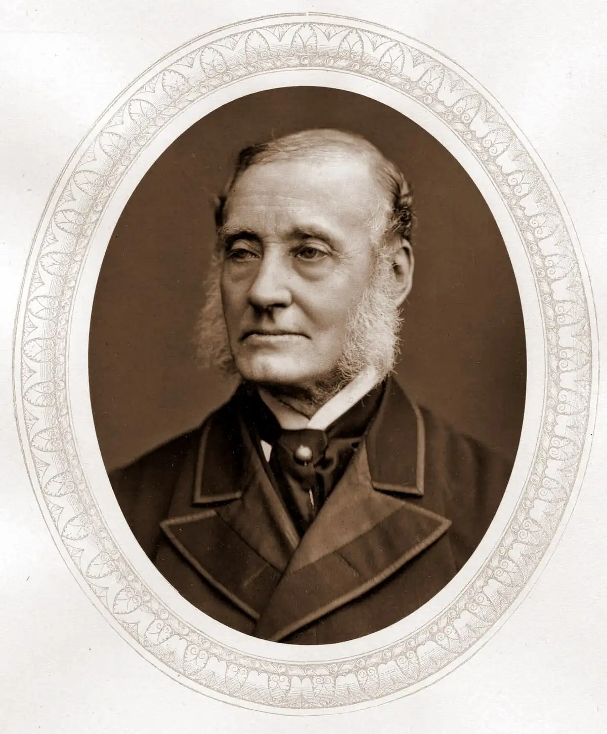 Sepia oval portrait of an elderly man with white side-whiskers in a dark coat with a velvet collar.