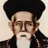 Colour portrait painting of an elderly man with a white beard, wearing a black Qing official hat with a red button and a beaded necklace.