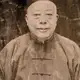 Sepia portrait of an older man in a small cap and a patterned silk jacket, on a cracked and stained print.