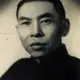 Sepia studio portrait of a man with short dark hair and a serious expression, in a dark high-collared jacket.