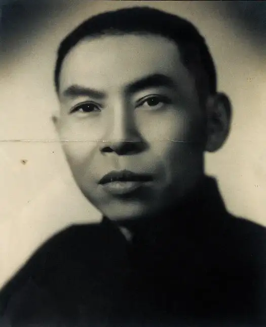 Sepia studio portrait of a man with short dark hair and a serious expression, in a dark high-collared jacket.