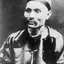 Black-and-white portrait of a man with a moustache wearing a skullcap and a dark silk jacket with toggle buttons.