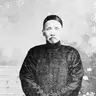Black-and-white full-length photograph of an older man in a long dark gown standing on garden steps, with Chinese calligraphy written over the picture.
