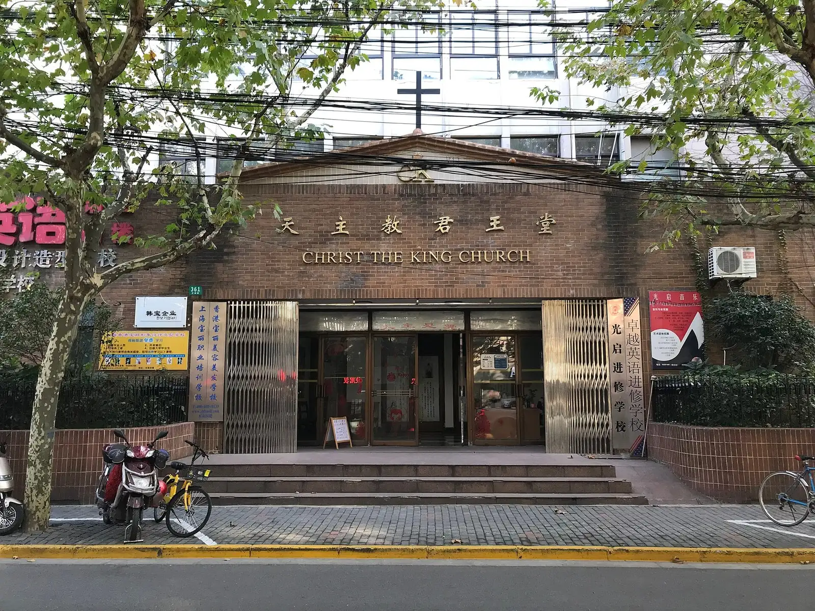 The low brick entrance of Christ the King Church on Julu Road, beneath leafy trees.