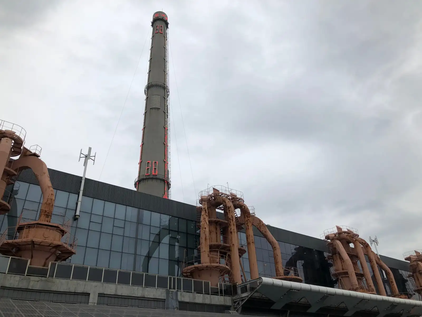 The tall chimney and industrial facade of the Power Station of Art beneath a cloudy sky.