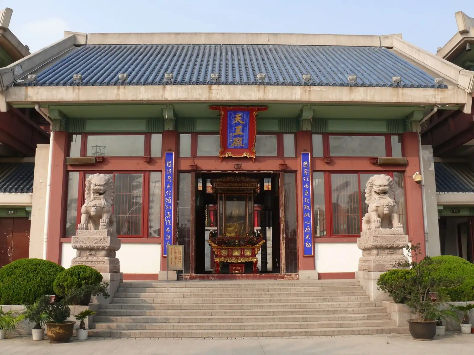 A hall at Qibao Temple, with red columns, a grey tiled roof and stone lions beside the stairs.