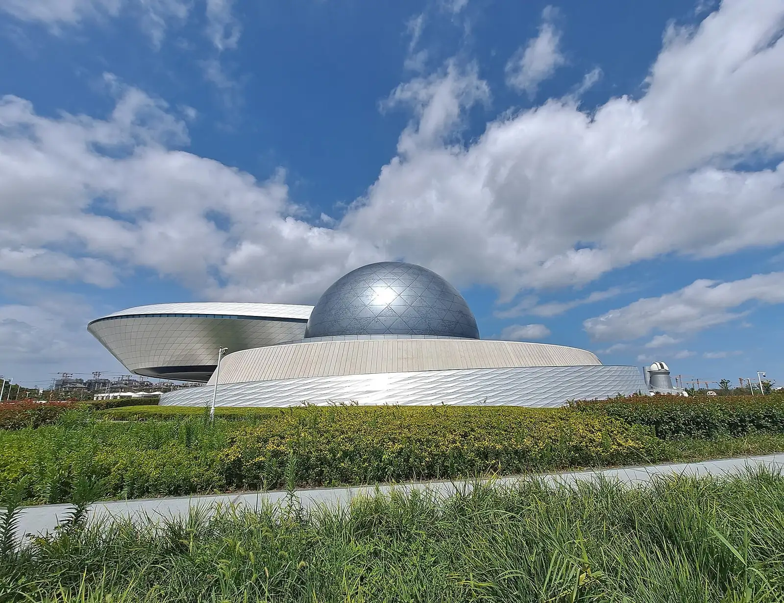 The curved silver buildings and dark dome of Shanghai Astronomy Museum beyond a green lawn.