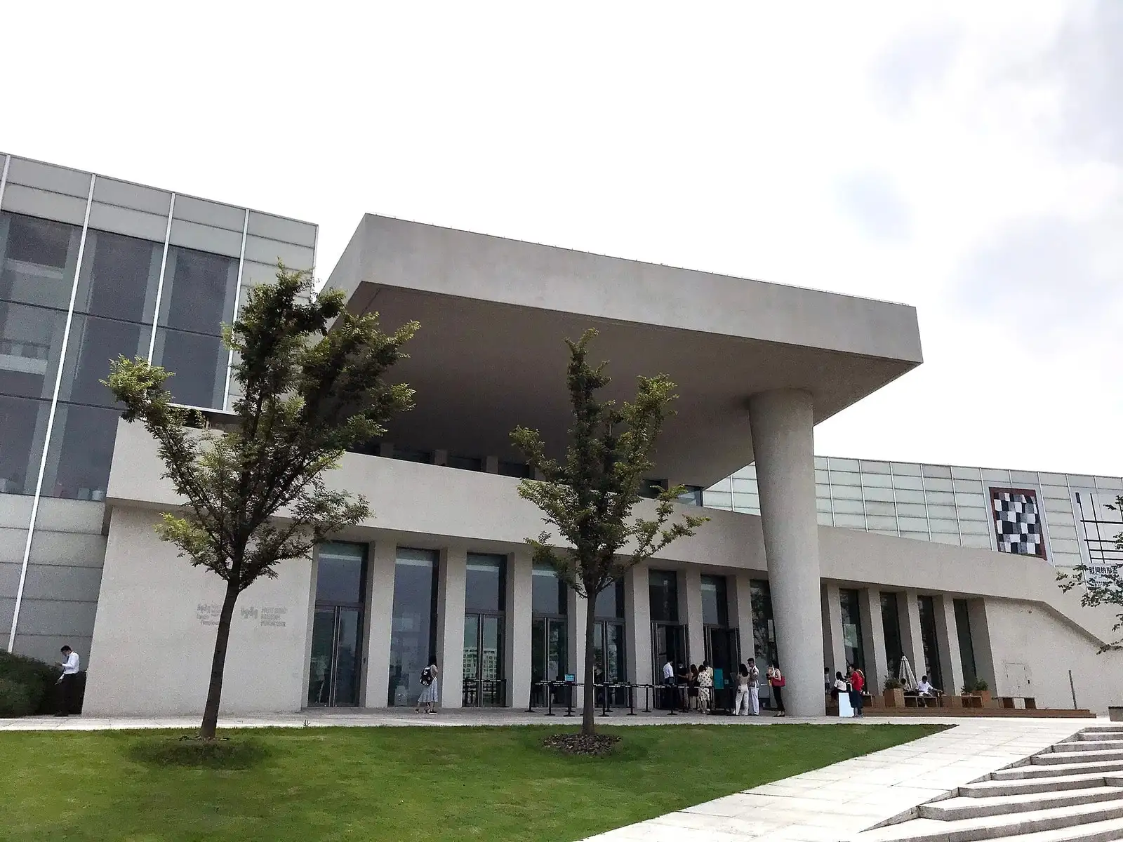 The entrance of West Bund Museum, with a broad concrete canopy and young trees in the forecourt.