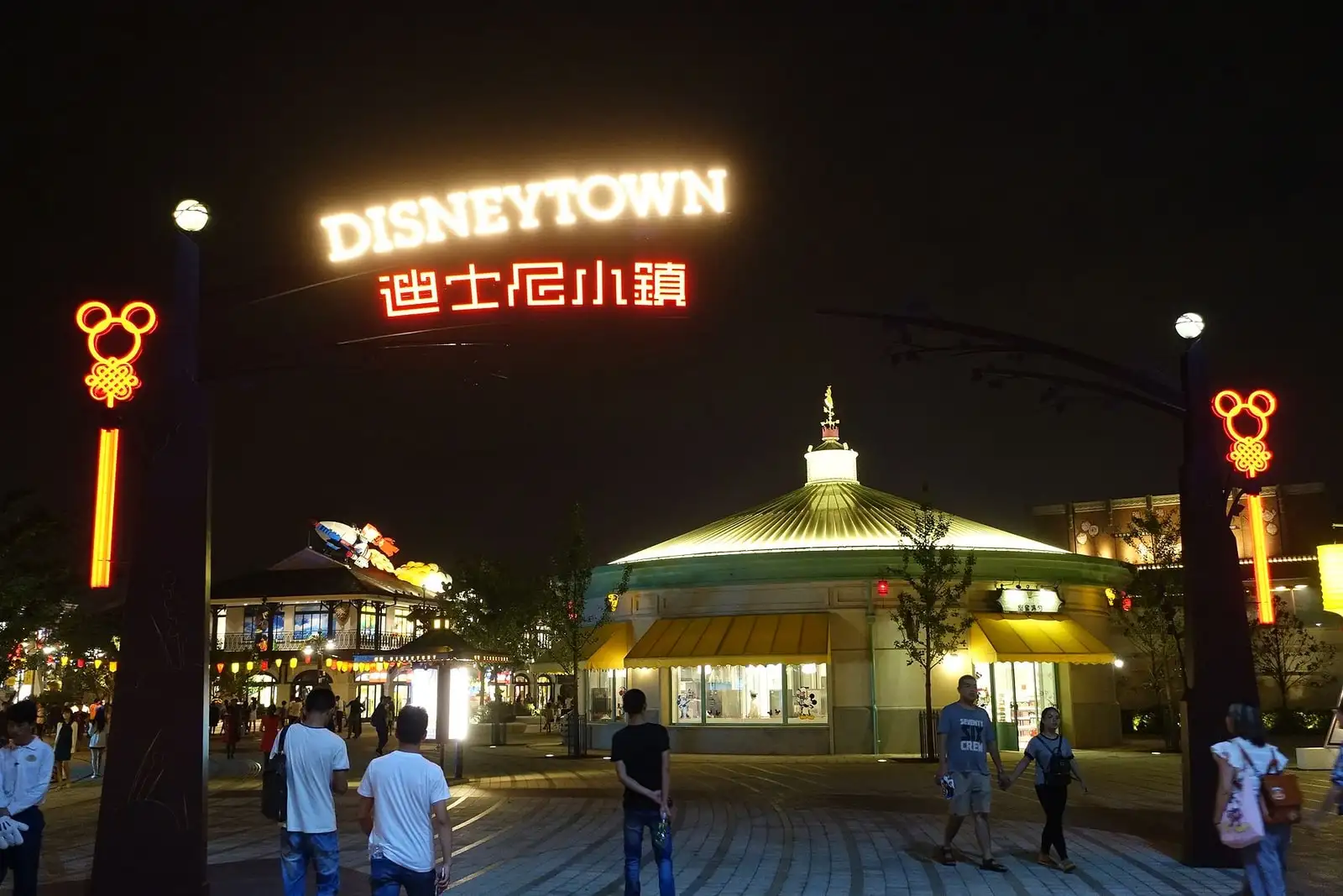 An illuminated Disneytown sign above a pavilion and visitors after dark.