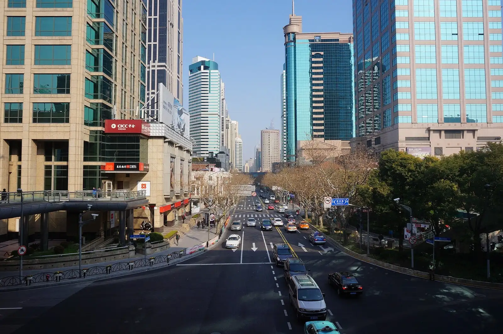Traffic along Middle Huaihai Road, with shops, roadside trees and office buildings.