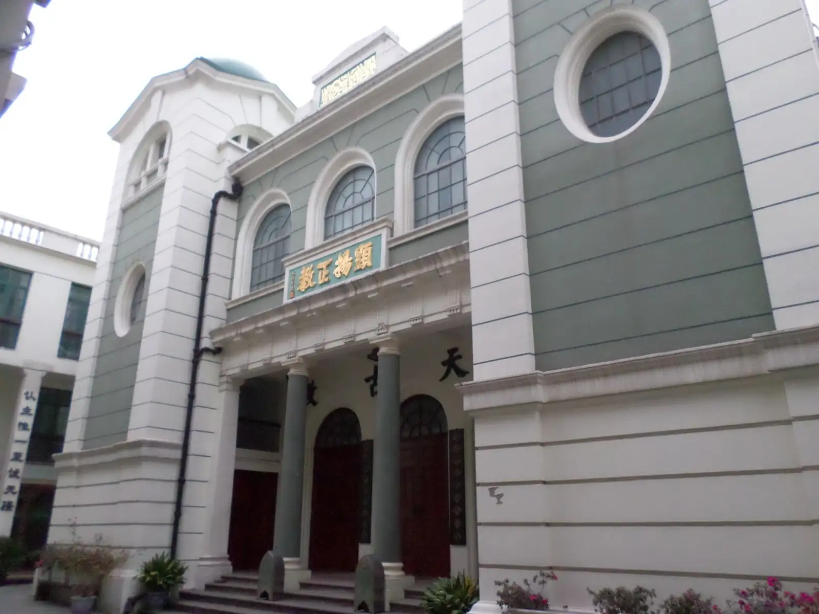 The pale street facade of Xiaotaoyuan Mosque, with arched windows, round windows and red entrance doors.